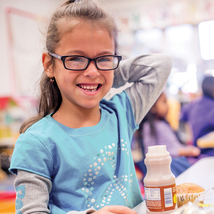 Little girl with breakfast in a school cafeteria.